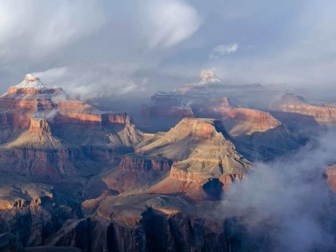 winter clouds and fog passing around a snow covered promentary within a vast mile deep canyon